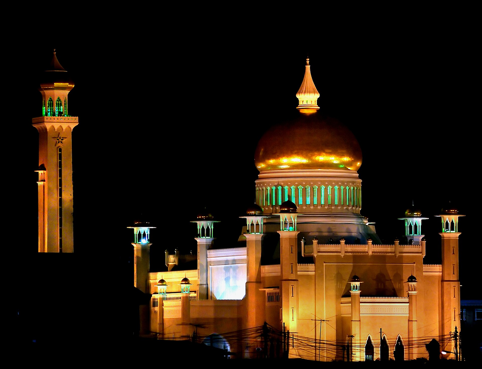 A grand mosque illuminated against the night sky, its domes and minarets reflected in water